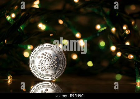 Iota cryptocurrency physical coin placed next to Christmas lights Stock Photo