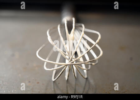 metal wire whisk with dough leftovers on a grey baking tray, close up view with copy space, selected focus and very narrow depth of field Stock Photo