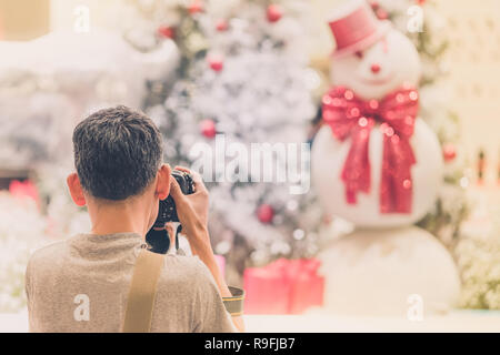 Photographer man take photo of decorated Christmas tree and a snowman. Stock Photo
