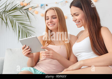 Young women rest together at home beauty care sitting on sofa browsing internet on digital tablet smiling happy Stock Photo