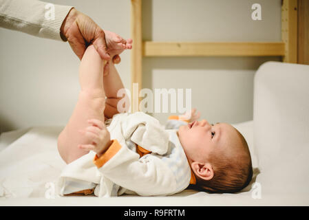 Mother changing diaper to baby, lifting her little legs. Stock Photo