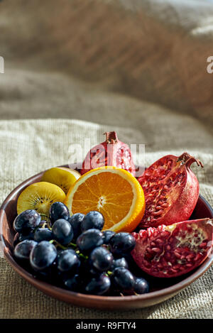 Autumn fruits. Overhead shot of a full plate of juicy, sliced fruits on wooden plate with grapes,orange, pomegranate and kiwi at the burlap cloth Stock Photo