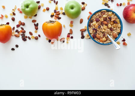 Reduce callories. Top view of healthy and useful breakfast, oats in bowl and fruits isolated on white background. Healthy snack or breakfast in the morning. Metal spoon in muesli Stock Photo