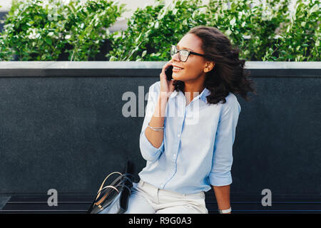 Female entrepreneur sitting outdoors using mobile phone Stock Photo