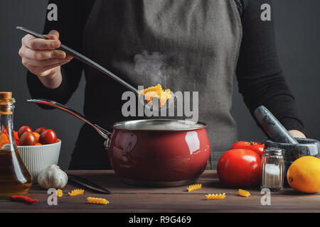 Cooking italian pasta in a pot in the kitchen, Chef preparing food, meal. Woman cook pulls out of the pan ready-made pasta fusilli. Stock Photo