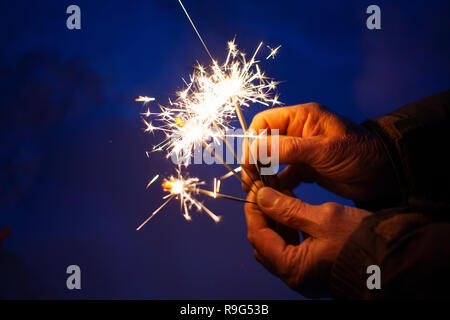 hands of elderly couple holding sparkles celebrating New Year Stock Photo