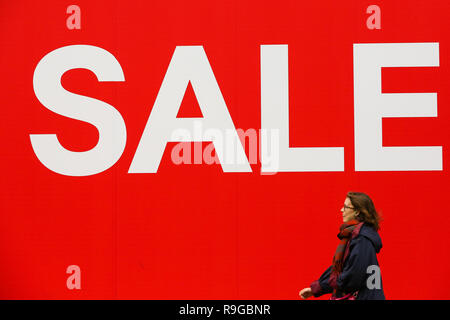 A woman is seen walking past a large SALE sign at H&M store on London'  Oxford Street. Last minute Christmas shoppers take advantage of  pre-Christmas bargains at Oxford Street in London. Fewer
