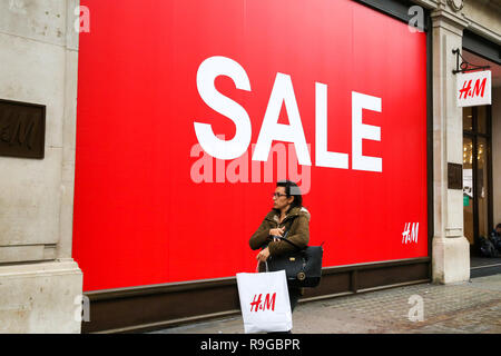 A woman is seen walking past a large SALE sign at H&M store while holding a  H&M shopping bag on London' Oxford Street. Last minute Christmas shoppers  take advantage of pre-Christmas bargains