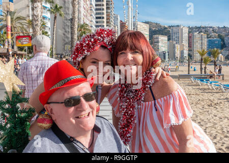 Benidorm, Costa Blanca, Spain, 24th December 2018. British holidaymakers escaping from the cold weather back home flood this popular resort during the Christmas holidays with this family adorned in tinsel and wearing bauble earings getting in the mood for the festivities. Sunbathers and swimmers enjoy the hot temps and calm weather on Levante beach today in Benidorm on the Costa Blanca coast. Temperatures were in the mid to high 20's Celsius today in this mediterranean hotspot. Credit: Mick Flynn/Alamy Live News Stock Photo