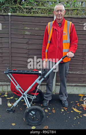 Royal Mail Postman, with mail trolley wearing orange jacket, delivering in Grappenhall, Warrington, Cheshire, England, UK Stock Photo