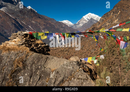Nepal, Namche Bazar, prayer flags flying from rough rocky chorten, Kongde Ri and Pachermo peak behind Stock Photo