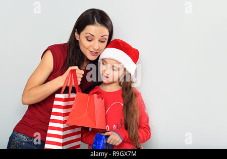 Happy surprising mother and cute daughter in santa clause hat opening the Christmas presents in package with excited face on blue studio background Stock Photo