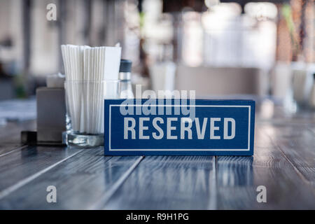 Closeup wooden blue white rectangular plate with word Reserved standing on gray vintage table in restaurant near to the serving, white paper napkins,  Stock Photo