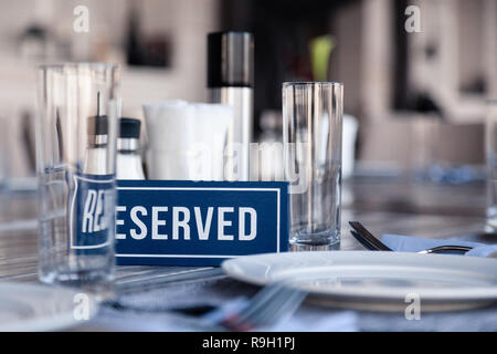 Closeup wooden blue white rectangular plate with word Reserved standing on gray vintage table in restaurant near to the serving, white paper napkins,  Stock Photo