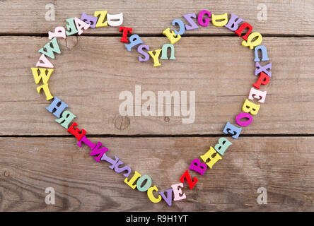 Frame of colored wooden letters in shape of heart on a wooden background Stock Photo