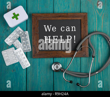 Medecine concept - Blackboard with text "We can help!", pills and stethoscope on blue wooden background Stock Photo