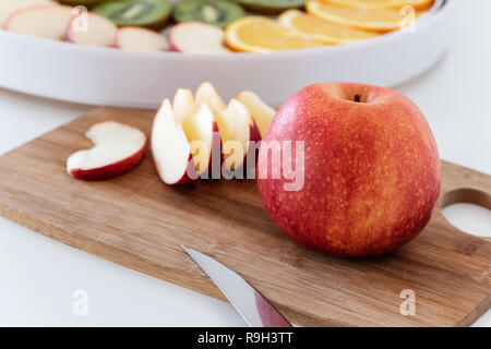 Cutting board with a knife, red apple and slices of apple. Behind is a dehydrator with slices of orange, kiwi and apples. Stock Photo