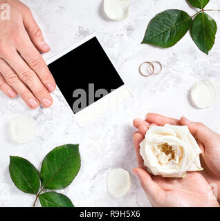 Blank photo frame, two wedding rings, bride and groom hands on white marble background Stock Photo