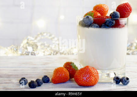 Panakota in a glass beaker with bright berries on a light wooden table. Stock Photo