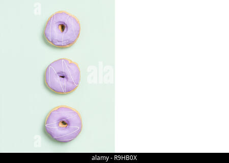 Three purple donuts on split color background modern design with copy space. Stock Photo