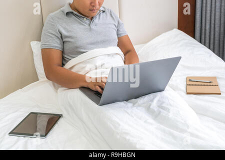 Young man working on laptop on white bed Stock Photo