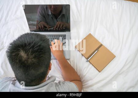 Rear view of young man lie on bed and working Stock Photo
