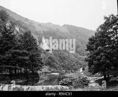 A late Victorian black and white photograph showing Dovedale, a valley in the Peak District of England. The land is now owned by the National Trust, and annually attracts a million visitors The valley was cut by the River Dove and runs for just over 3 miles (5 km) between Milldale in the north and a wooded ravine near Thorpe Cloud and Bunster Hill in the south. In the wooded ravine, a set of stepping stones cross the river, and there are two caves known as the Dove Holes. Stock Photo