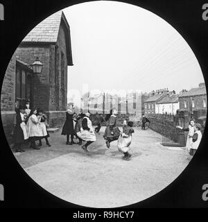 A late Victorian photograph showing a group of school children in an English school playground. There are some girls skipping with a skipping rope, whilst other children look on. Stock Photo