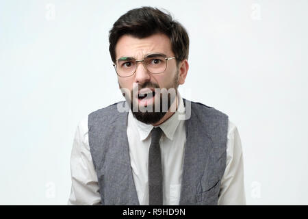 Suspicious bearded man looks doubtfully, being indecisive, makes grimace, tries to find solution. Stock Photo