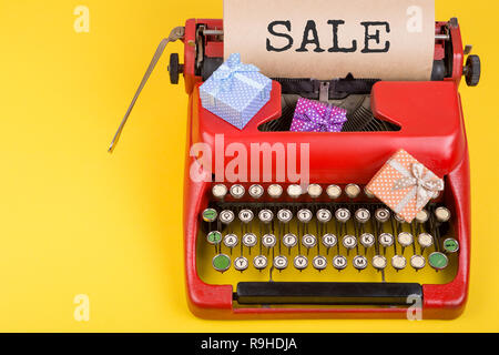 Holidays concept - red typewriter with craft paper with text "Sale", gift boxes on yellow background Stock Photo