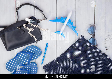 Travel concept - summer women's fashion with blue bag, sunglasses, flip flops, nail polish and little airplane on white wooden background Stock Photo