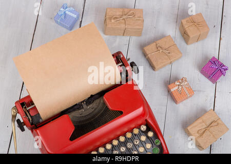 Holidays concept - red typewriter with blank craft paper, gift boxes on white wooden background Stock Photo