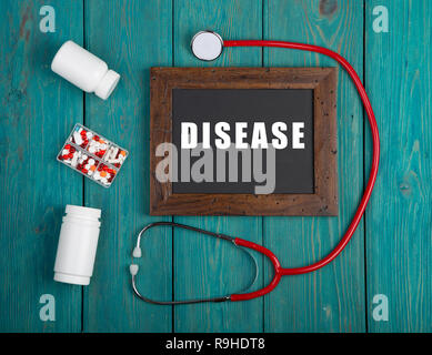 Medecine concept - Blackboard with text 'Disease', book, pills and stethoscope on blue wooden background Stock Photo