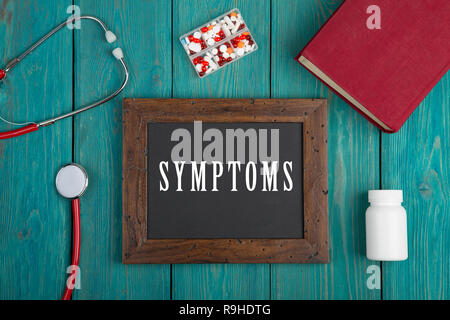 Medecine concept - Blackboard with text 'Symptoms', book, pills and stethoscope on blue wooden background Stock Photo