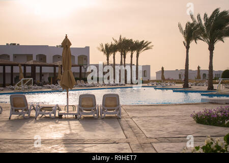 beautiful view of the pool with sun loungers on the background of white hotel, palm trees and azure sea. Wallpaper, postcard Stock Photo