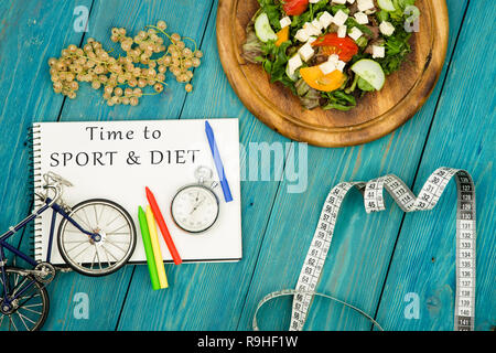 bicycle model, salad of fresh vegetables, notepad with text "Time to SPORT & DIET", stopwatch and tape measure on a blue wooden table Stock Photo