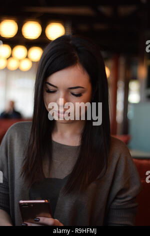 portrait of a smiling beautiful girl with dimples on the cheeks in a cozy cafe against the window and bokeh. young woman is reading a message in the p Stock Photo