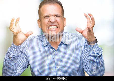 Middle age arab business man over isolated background Shouting frustrated with rage, hands trying to strangle, yelling mad Stock Photo