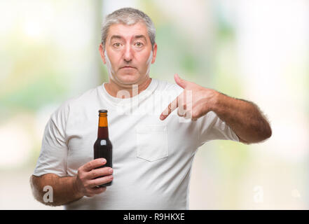 Handsome senior man drinking beer bottle over isolated background with surprise face pointing finger to himself Stock Photo