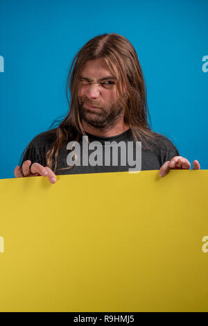 Male portrait displaying a funny wink sign while holding a yellow banner. Copyspace available for advertise message or information Stock Photo