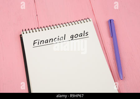 Notepad with text "Financial goals" and pen on pink wooden table Stock Photo
