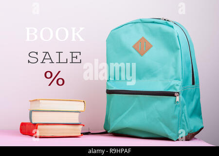 Blue school backpack and books is on a pink wooden table on pink background with text "Book sale %" Stock Photo