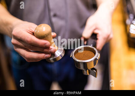 Man is using a tamper to press freshly ground morning coffee into a coffee tablet Stock Photo