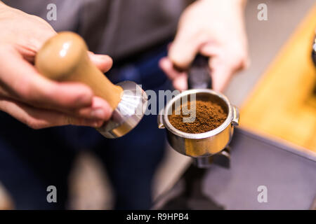 Man is using a tamper to press freshly ground morning coffee into a coffee tablet Stock Photo