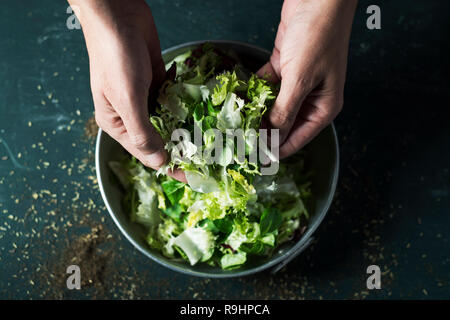 closeup of a young caucasian man about to prepare a salad with a mix of different salad leaves, like romaine lettuce, endive or arugula, in a rustic m Stock Photo