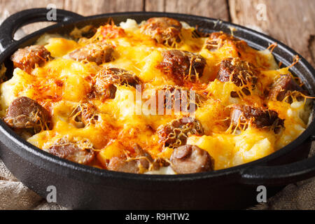 Hot Jolean's potato casserole, smoked sausages with cheese sauce close-up in a frying pan on the table. horizontal Stock Photo