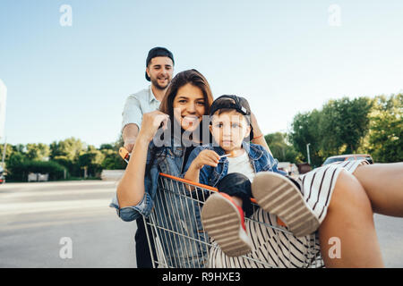 Young dad carries mom and son in a cart on the parking lot Stock Photo