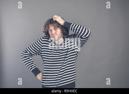 Puzzled guy with messy hair, frowning and looking unsatisfied scratching head, thinking deeply about something on grey wall background. Human facial e Stock Photo