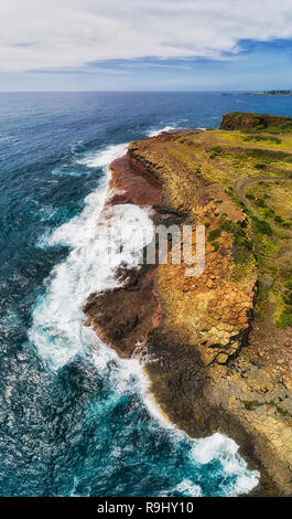 Hexagonal basalt stone pinnacles on waterfront of Bombo quarry site in Kiama town on Australian pacific coast - vertical aerial panorama from water su Stock Photo