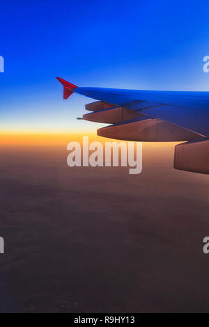 East and distant horizon at sunrise seen high in the sky from on board of flying airplane and fragment of wing with jet engines. Stock Photo